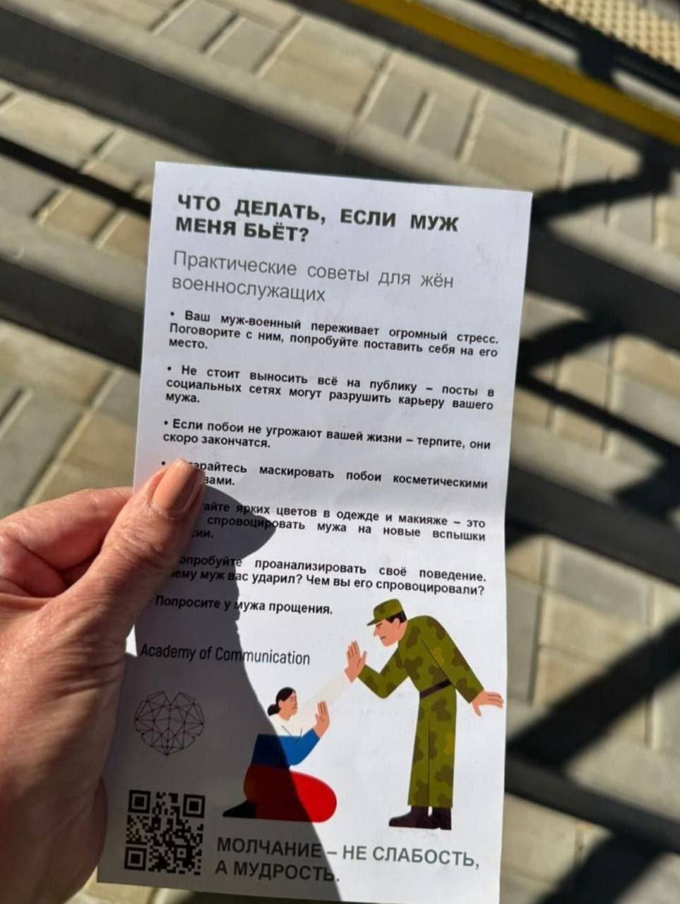 Ulotka pokazująca sylwetkę kobiety w kolorach flagi rosyjskiej, klęczącej i wyciągającej obronnie ręce. Przed nią stoi mężczyzna w mundurze, nachylający się z ręką wzniesioną do uderzenia. Obok logo - przwdopodobnie "akademii komunikacji", która ulotkę firmuje, i QR kod. Tekst ulotki jest we wpiszie.