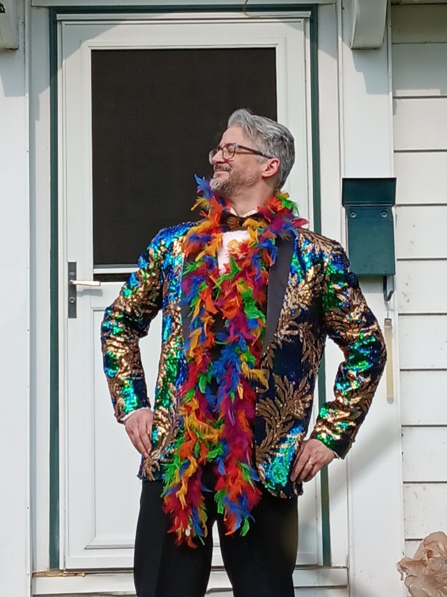 man in a sequined tuxedo jacket and rainbow feathered boa