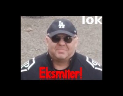 Oblech w czarnych brylkach i dziwacznym kostiumie, świńską mordą wprost do widza. Na tle dekoltu krwawiącymi czerwono literami napis "Eksmiter!"
